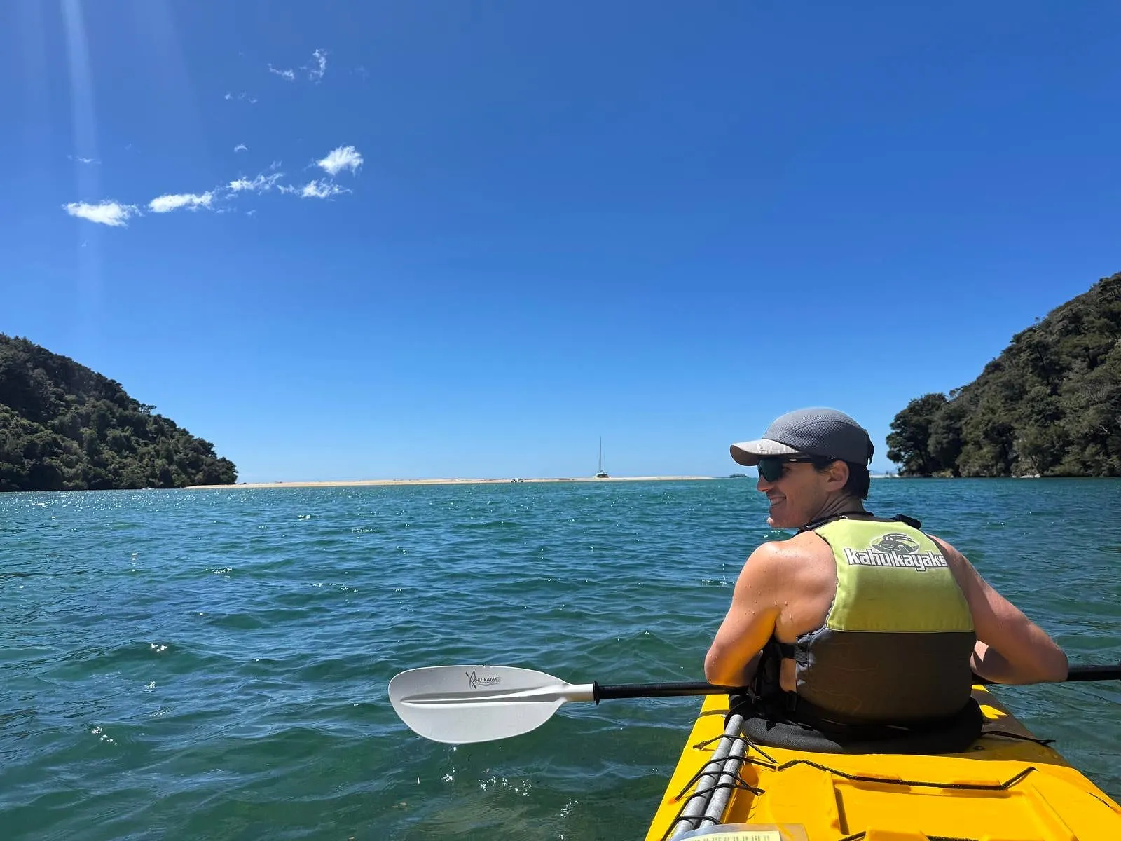 Sea kayaking through a sheltered turquoise bay between bush-covered headlands — a typical free weekend for a Waikato Hospital plastic surgery fellow in Aotearoa New Zealand